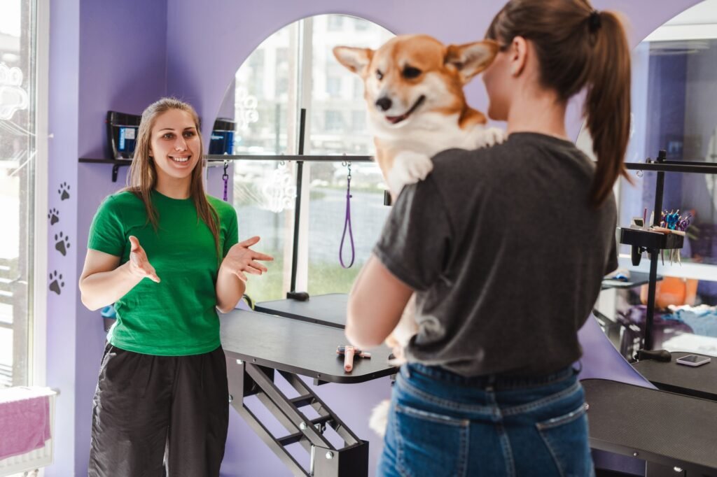 Smiling woman groomer talking with lady owner of cute corgi dog after grooming