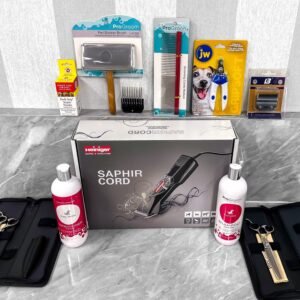 The image shows a variety of dog grooming tools and supplies on a marble countertop. Items include a Saphir Cord clipper in its box, grooming scissors, combs, a claw trimmer, and bottles of cleaning solution, neatly arranged.