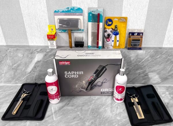 The image shows a variety of dog grooming tools and supplies on a marble countertop. Items include a Saphir Cord clipper in its box, grooming scissors, combs, a claw trimmer, and bottles of cleaning solution, neatly arranged.