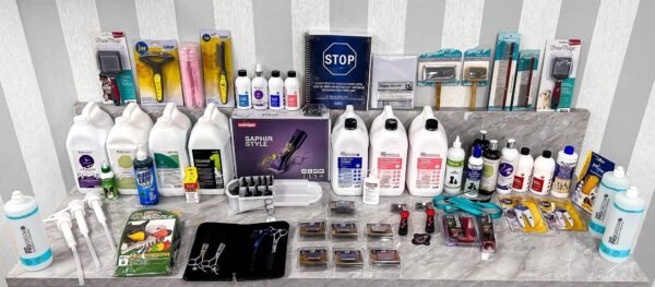 An Ultimate Dog Grooming Starter Bundle is organized on a marble countertop, featuring shampoos, trimmers, brushes, combs, scissor sets, and grooming tools. A "STOP" sign and several packaging boxes are also present.