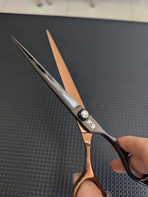 K9 Trailer Rentals A hand holds the 7" Straight Pet Grooming Scissors—crafted from premium 440C Japanese steel, featuring black and gold handles—against a textured black background.