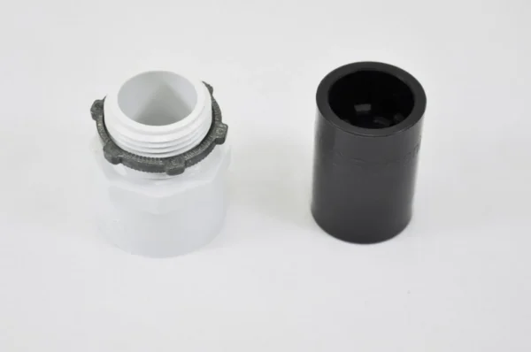 K9 Trailer Rentals A white plastic threaded connector with a gray ring next to a black cylindrical cap, both placed on a plain white surface.