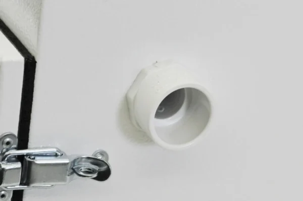K9 Trailer Rentals Close-up of a white plastic pipe fitting or vent protruding from a white wall, with a metal latch and hinge visible in the lower left corner.