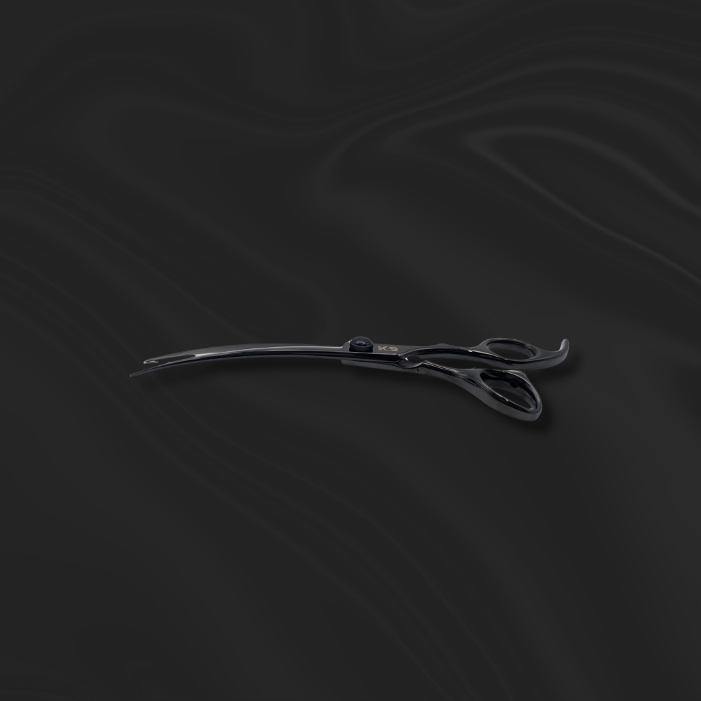 K9 Trailer Rentals The 7″ Black 440C Steel K9 Curve Scissor rests on a dark, softly matte wavy surface, highlighting its sleek curved black design.
